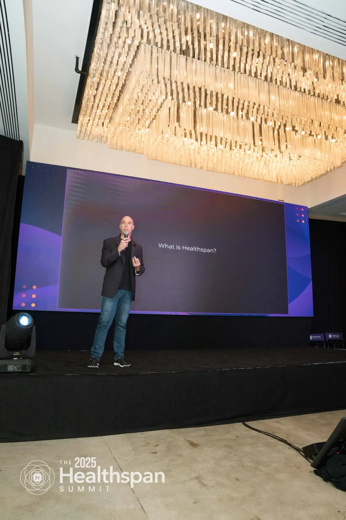 Elias Arjan speaking on the Healthspan Summit stage beneath a chandelier