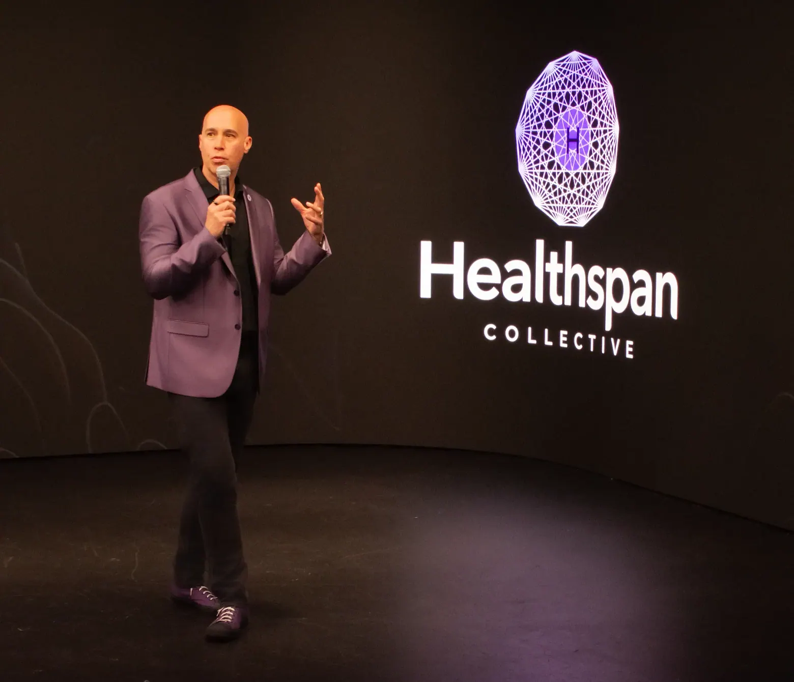 Elias Arjan speaking on a dark stage beside the Healthspan Collective emblem